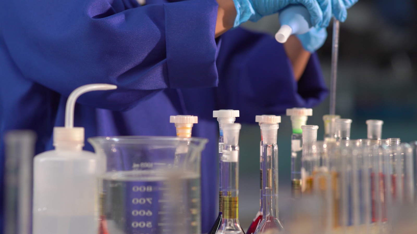 Laboratory technician pipetting samples among beakers and test tubes