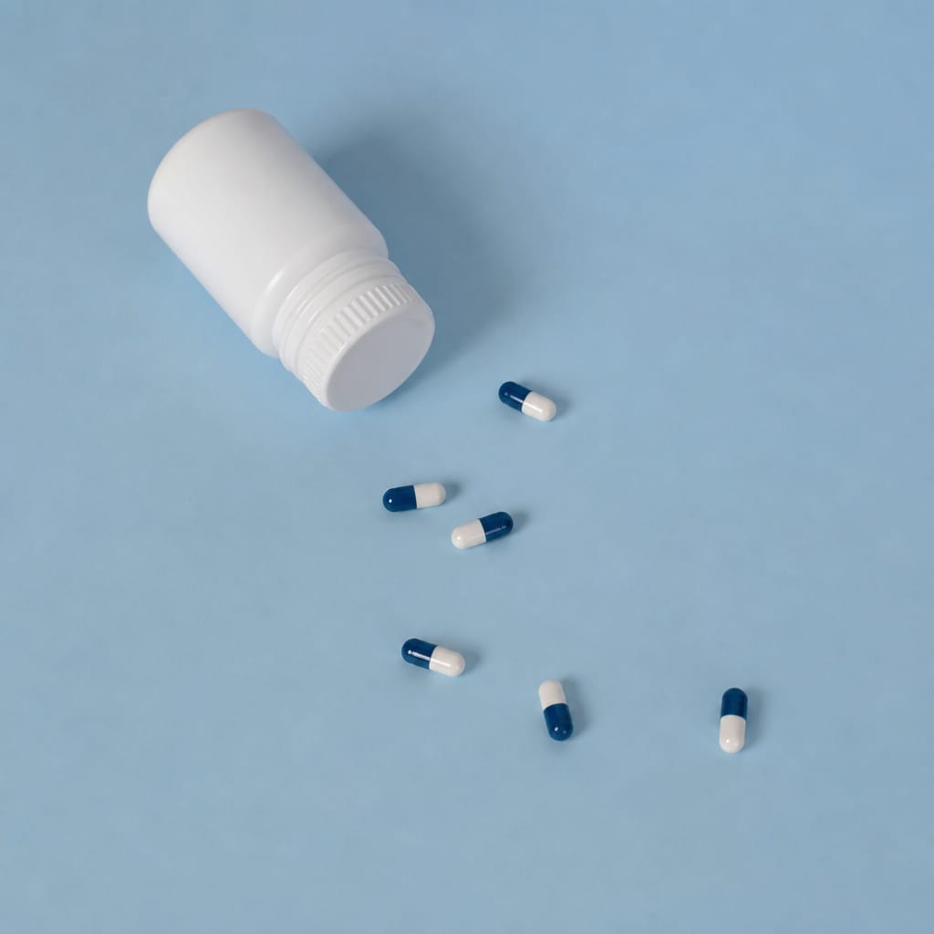 Blue and white capsules beside a white medicine bottle